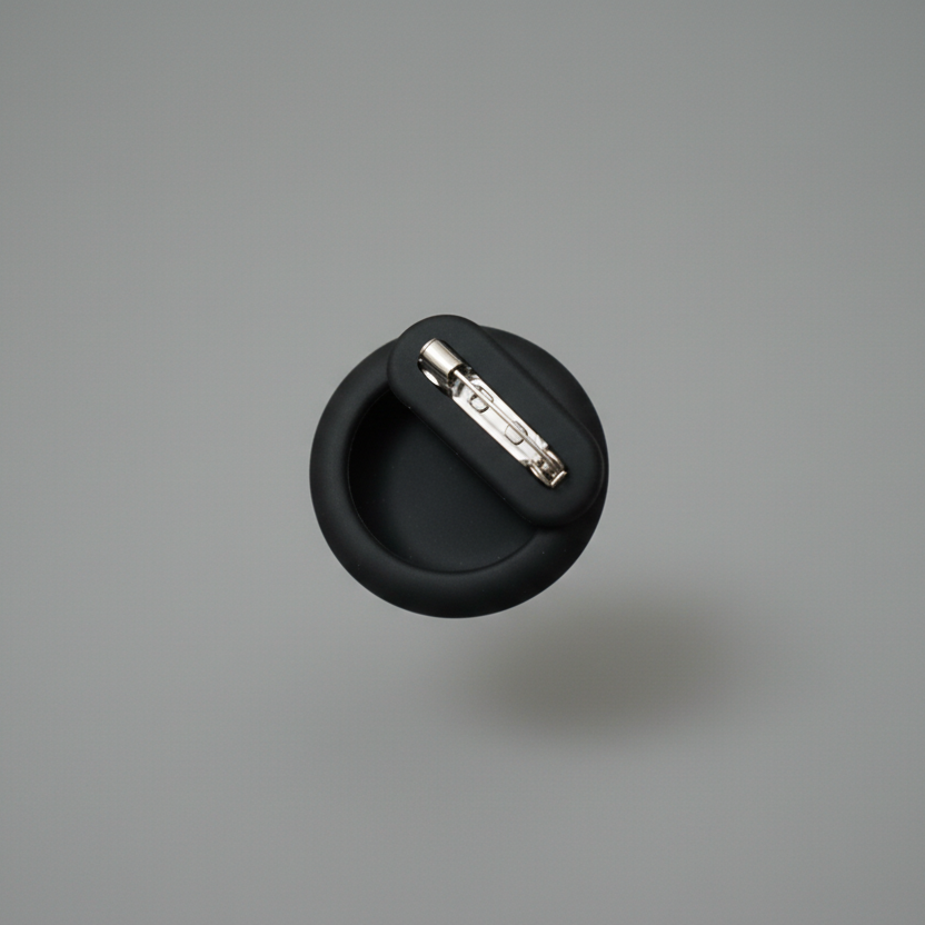 Round black pet accessory pin with metal clasp on grey background